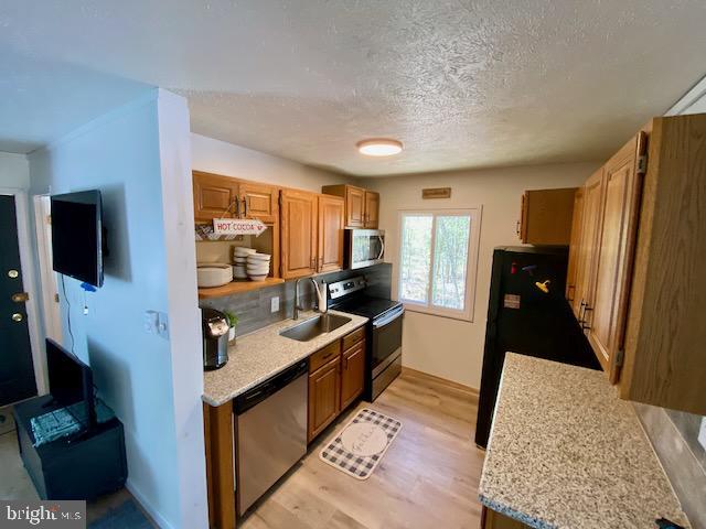 kitchen with stainless steel appliances, light countertops, light wood-style flooring, a sink, and brown cabinets