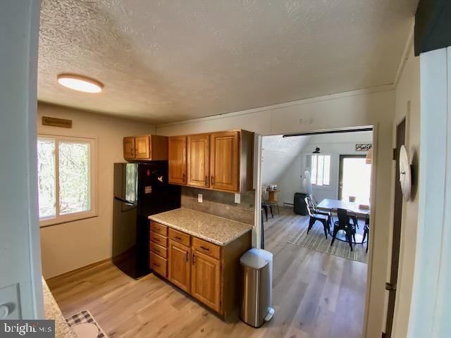 kitchen featuring brown cabinetry, a textured ceiling, freestanding refrigerator, light wood-style floors, and backsplash