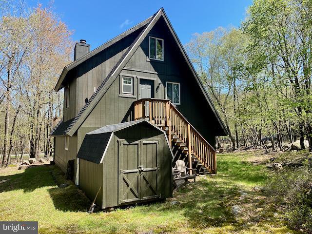rear view of house with a chimney, a yard, an outdoor structure, and a storage unit