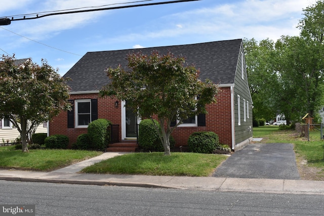 cape cod home featuring brick siding, roof with shingles, and a front lawn