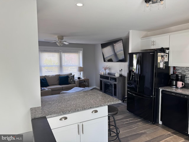 kitchen with black appliances, ceiling fan, dark wood-type flooring, white cabinetry, and a breakfast bar