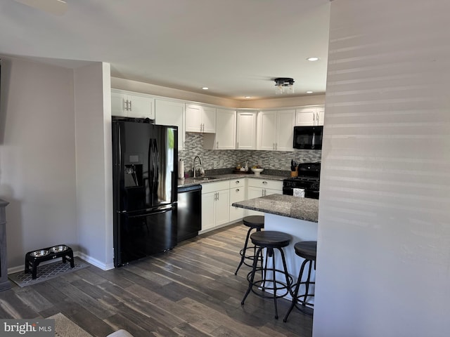 kitchen with black appliances, dark wood-style flooring, a breakfast bar area, white cabinetry, and a sink