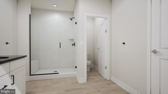 bathroom featuring wood finished floors, a stall shower, toilet, baseboards, and recessed lighting