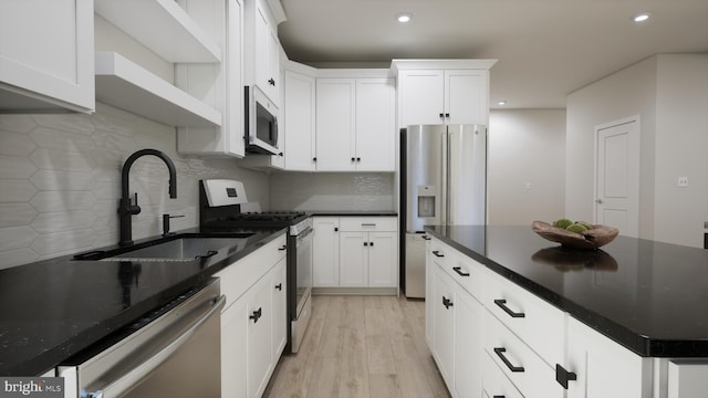 kitchen with appliances with stainless steel finishes, a sink, dark countertops, light wood finished floors, and recessed lighting