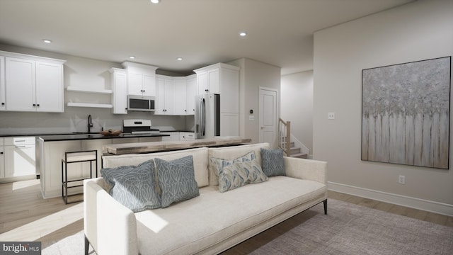 kitchen featuring appliances with stainless steel finishes, a sink, light wood-type flooring, open shelves, and white cabinetry