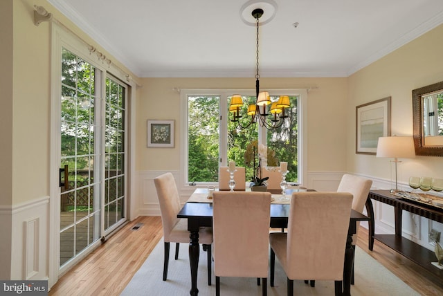 dining room with a chandelier, light wood-style floors, a decorative wall, a wainscoted wall, and ornamental molding