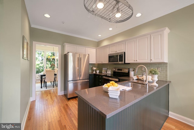 kitchen with appliances with stainless steel finishes, a sink, white cabinets, ornamental molding, and tasteful backsplash