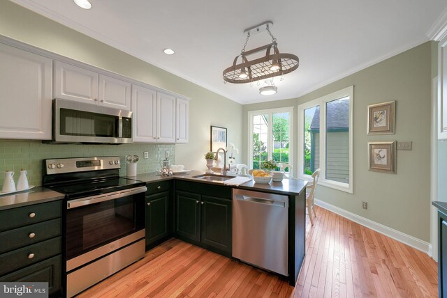 kitchen featuring appliances with stainless steel finishes, a sink, white cabinets, crown molding, and a peninsula