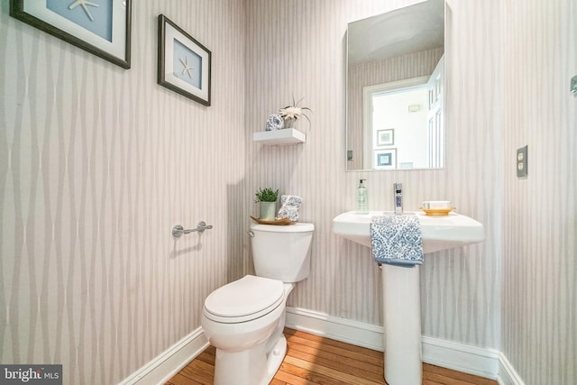 half bathroom featuring wood finished floors, toilet, baseboards, and wallpapered walls