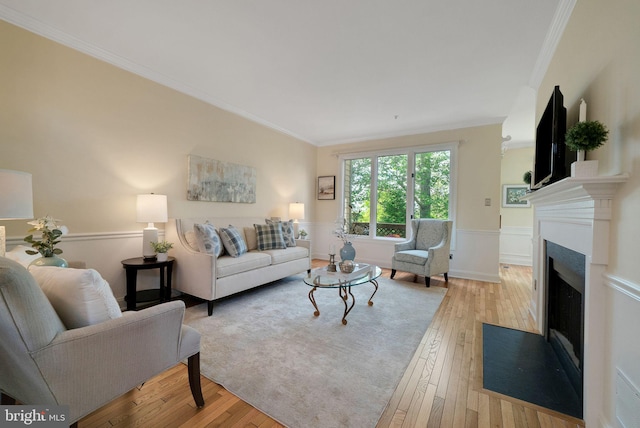 living room featuring ornamental molding, a fireplace with flush hearth, wainscoting, and light wood-style floors