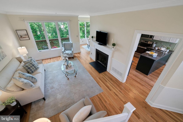 living room with crown molding, light wood finished floors, a fireplace with flush hearth, and baseboards