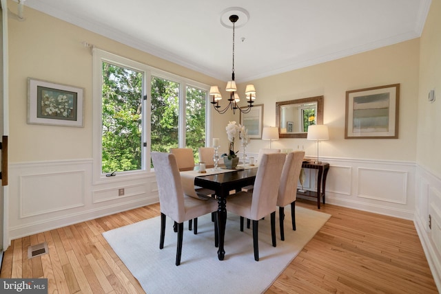 dining space featuring a chandelier, a decorative wall, light wood finished floors, a wainscoted wall, and ornamental molding
