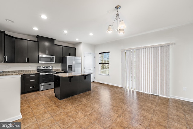 kitchen with appliances with stainless steel finishes, dark cabinets, a kitchen island, a kitchen breakfast bar, and decorative light fixtures