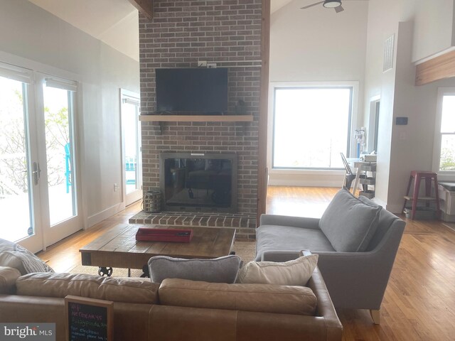 living area with high vaulted ceiling, a brick fireplace, wood finished floors, baseboards, and a ceiling fan