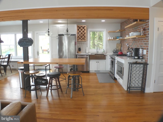 kitchen with stainless steel appliances, a sink, white cabinetry, hanging light fixtures, and light countertops