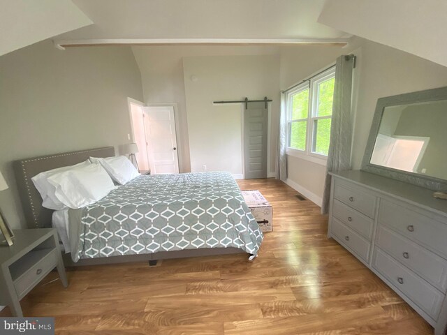 bedroom featuring vaulted ceiling, light wood-style flooring, a barn door, and baseboards