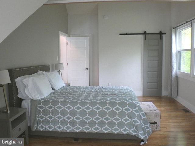 bedroom with wood finished floors, a barn door, baseboards, and vaulted ceiling