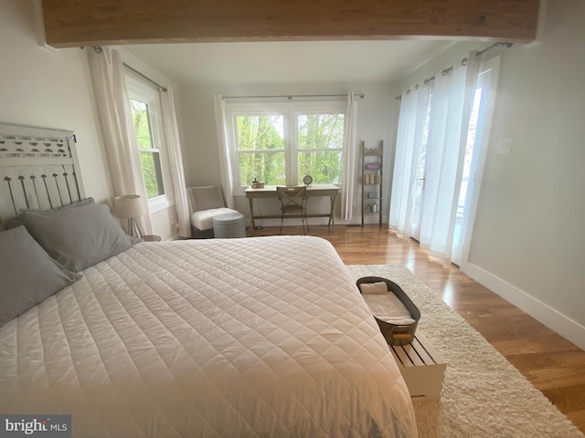 bedroom with beam ceiling, baseboards, and wood finished floors