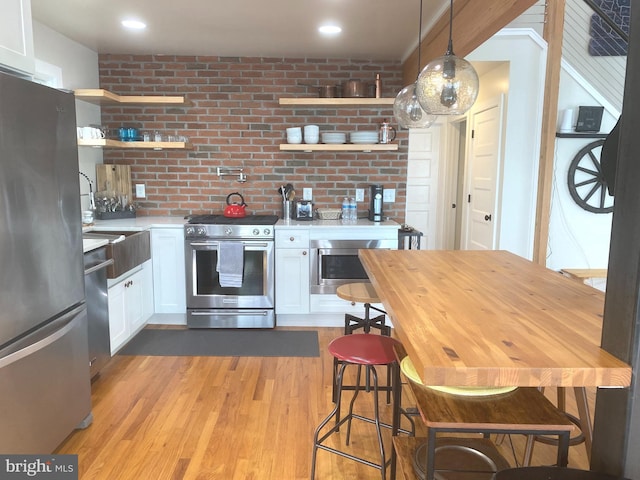 kitchen with stainless steel appliances, open shelves, white cabinets, light wood-style floors, and hanging light fixtures