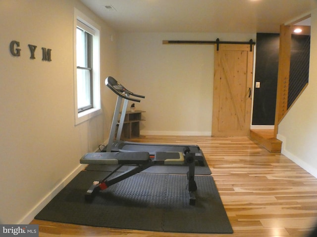 workout area featuring wood finished floors, a barn door, and baseboards