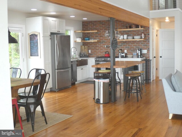 kitchen with stainless steel appliances, open shelves, a sink, light wood-style floors, and light countertops