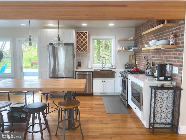 kitchen with stainless steel appliances, a sink, light countertops, light wood-style floors, and white cabinets