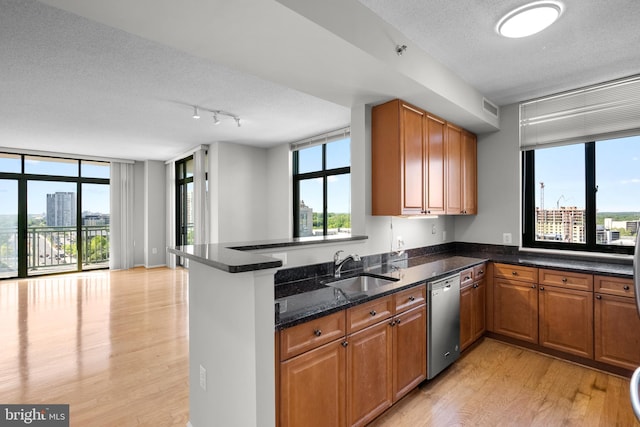 kitchen with stainless steel dishwasher, a textured ceiling, a sink, light wood-style floors, and brown cabinets