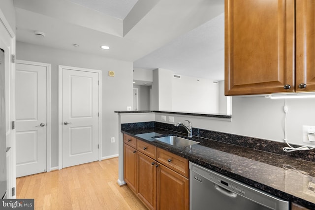 kitchen featuring dishwasher, a sink, light wood finished floors, dark stone countertops, and brown cabinetry