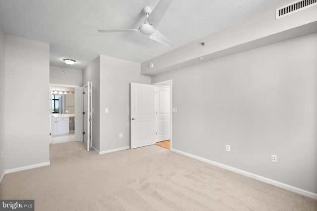 unfurnished bedroom featuring light carpet, baseboards, ensuite bath, and a textured ceiling