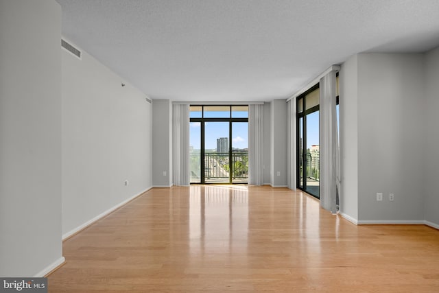 spare room with expansive windows, wood finished floors, baseboards, and a textured ceiling