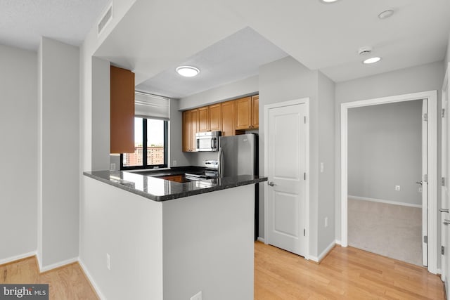 kitchen with appliances with stainless steel finishes, light wood-style floors, a peninsula, and baseboards