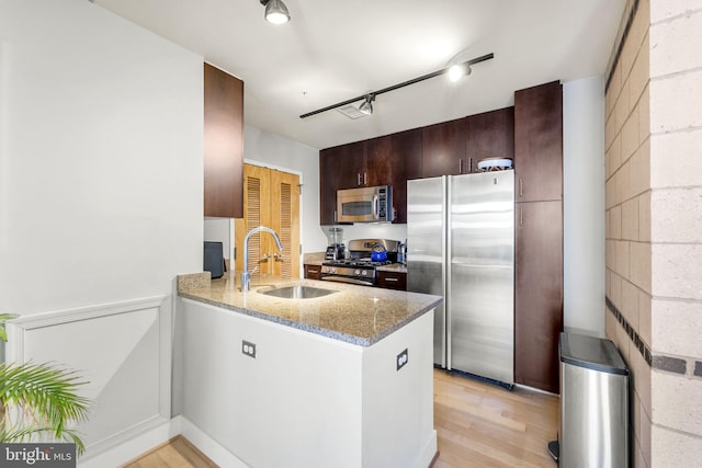 kitchen with appliances with stainless steel finishes, a sink, light wood-style flooring, a peninsula, and light stone counters