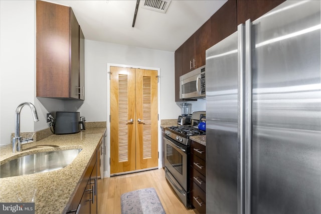 kitchen with stainless steel appliances, a sink, light wood-style flooring, and light stone counters