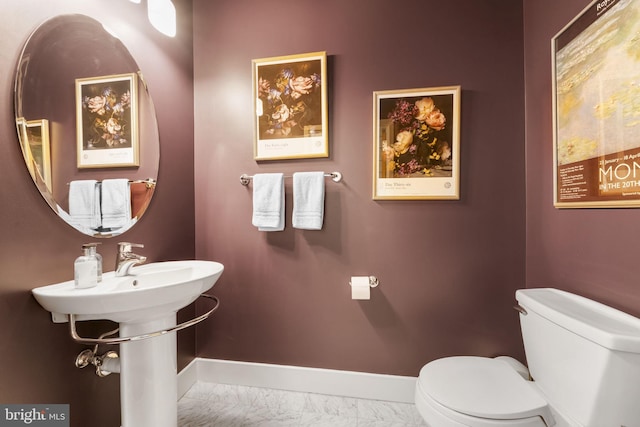 half bathroom with baseboards, toilet, and marble look tiles