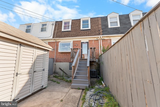 8031 Stratman Rd, Baltimore, MD 21222 - rear view of house featuring brick siding, a shingled roof, mansard roof, central AC unit, and an outbuilding