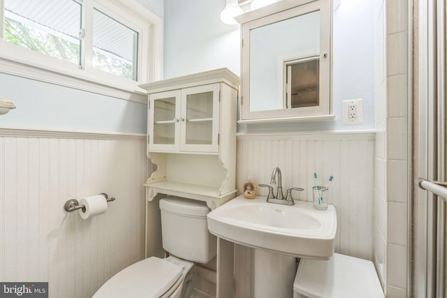 half bath featuring a wainscoted wall and toilet