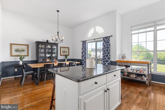 kitchen featuring dark wood-style flooring, a chandelier, white cabinets, a center island, and a breakfast bar