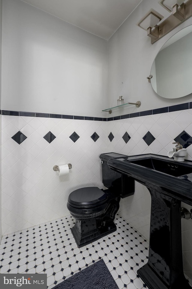 half bathroom with tile walls, a wainscoted wall, toilet, and tile patterned flooring