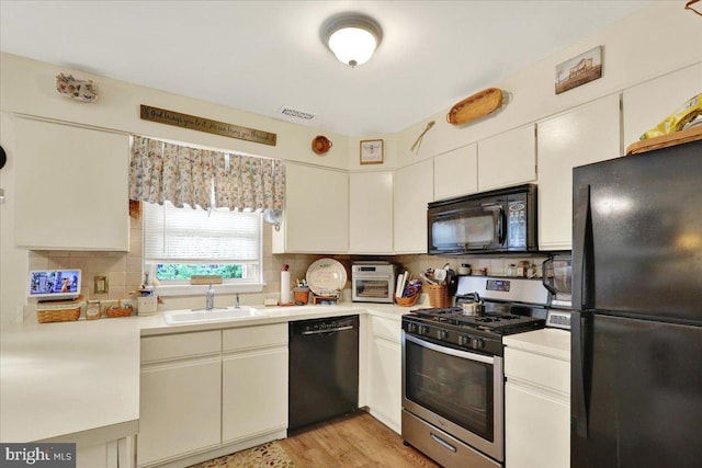 kitchen featuring black appliances, a sink, light countertops, decorative backsplash, and white cabinets