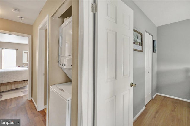 laundry room with stacked washer / drying machine, wood finished floors, and baseboards