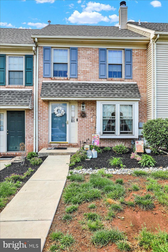 multi unit property with brick siding, a chimney, and a shingled roof
