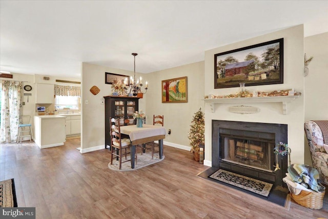 dining area with a chandelier, wood finished floors, a fireplace with flush hearth, and baseboards