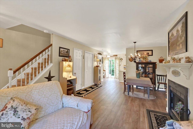 living area featuring a chandelier, wood finished floors, stairway, and a fireplace with flush hearth