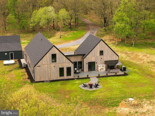 back of property with a fire pit, a shingled roof, and a lawn