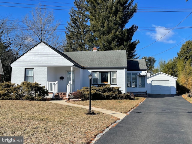 view of front facade with brick siding, a detached garage, a front yard, and a chimney