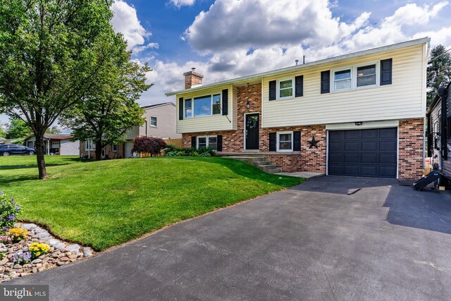 split foyer home with driveway, an attached garage, brick siding, a chimney, and a front lawn
