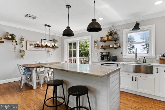 kitchen with a sink, ornamental molding, white cabinets, open shelves, and a center island