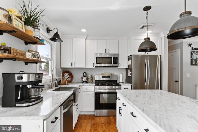 kitchen with stainless steel appliances, a sink, white cabinets, pendant lighting, and light stone countertops