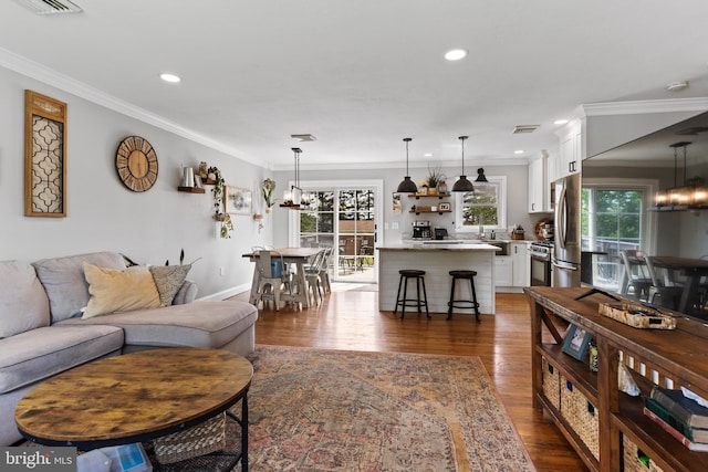 living area featuring a chandelier, dark wood-type flooring, ornamental molding, recessed lighting, and baseboards