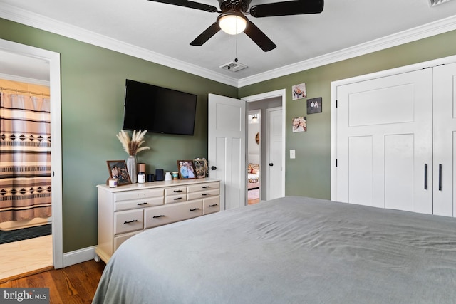 bedroom featuring dark wood finished floors, crown molding, baseboards, ensuite bathroom, and a ceiling fan